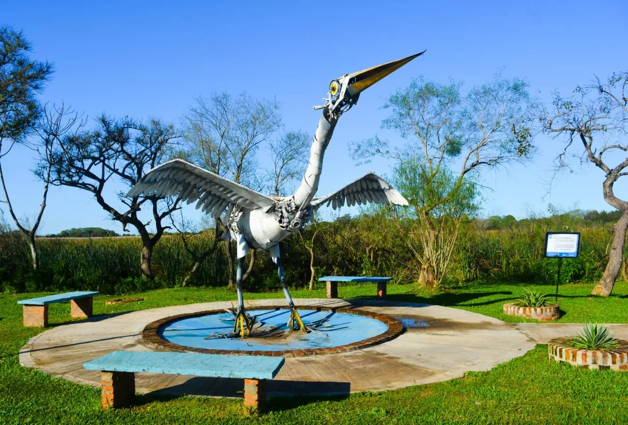 Gran escultura metálica de una garza con las alas abiertas sobre una fuente