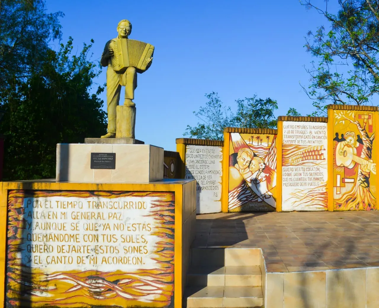 Estatua de un acordeonista con murales y versos de chamamé